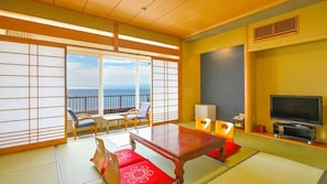 Una habitación con suelo de tatami, una mesita, un sofá, un televisor y vistas al mar.