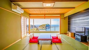 Una habitación con suelo de tatami, una mesa baja con cojines, un televisor y vista al mar.