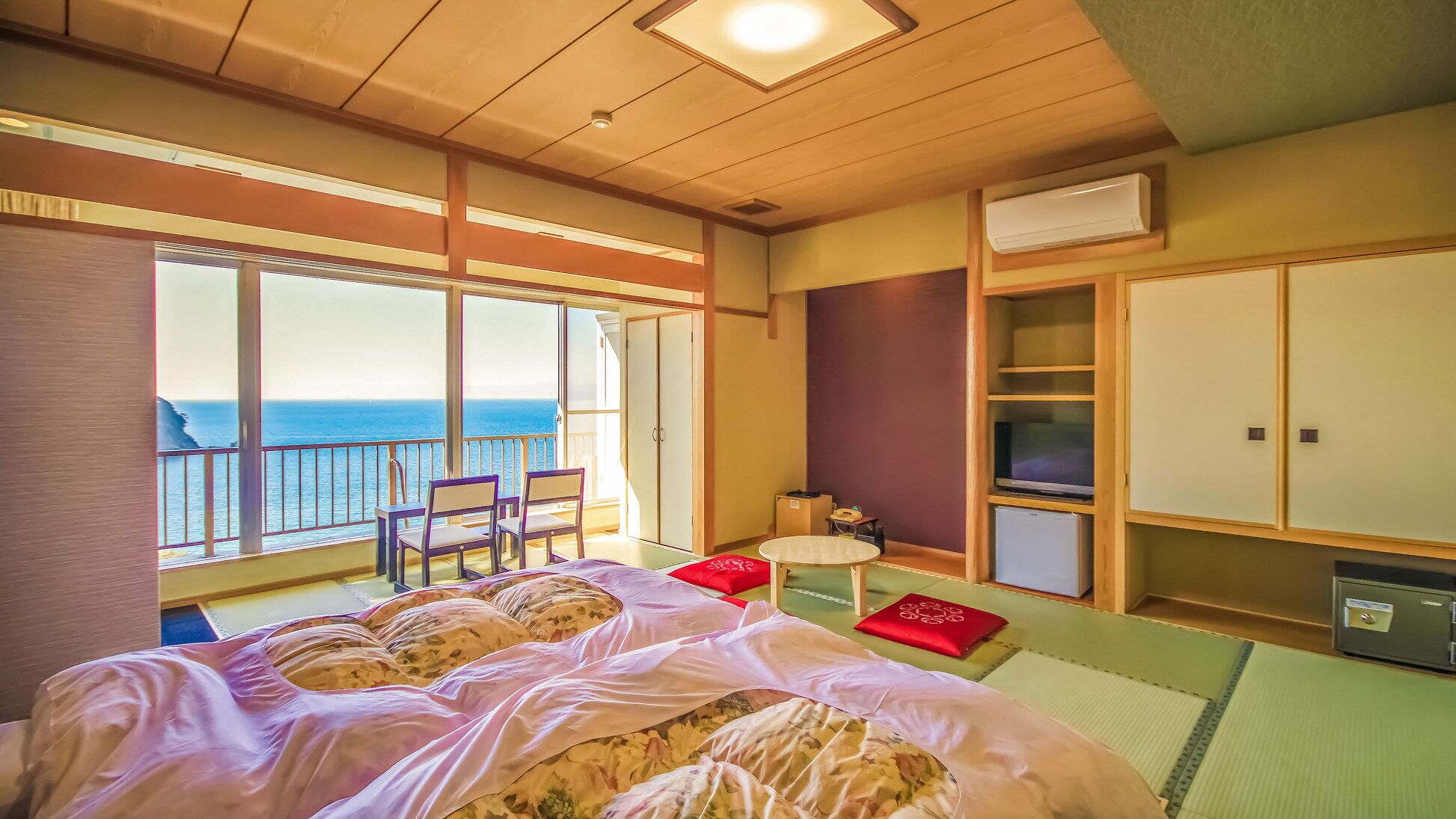 Een kamer met een bed, een klein tafeltje, een televisie en een kledingkast. Er is een balkon met uitzicht op zee.