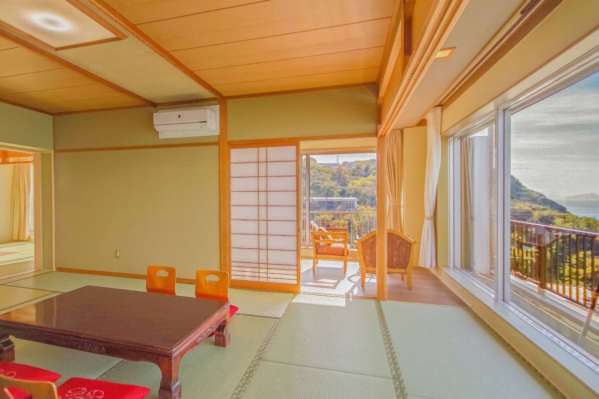 Una habitación tradicional japonesa con suelo de tatami, una mesa baja y puertas correderas que dan a un balcón con vistas.