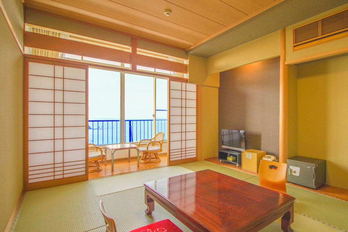 Una habitación japonesa tradicional con suelo de tatami, una mesa baja, un televisor y puertas correderas con vistas.