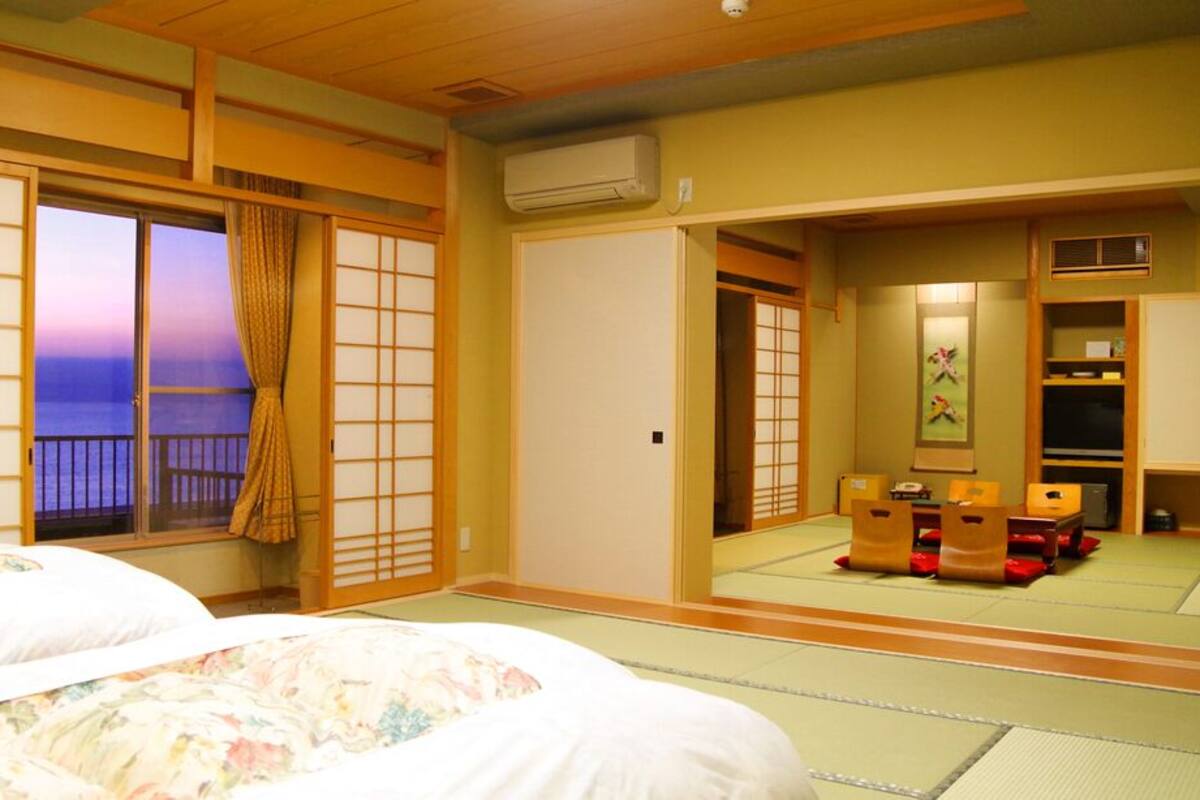 Una habitación japonesa tradicional con suelo de tatami, puertas correderas, una cama con ropa de cama floral, un televisor y vista al mar.
