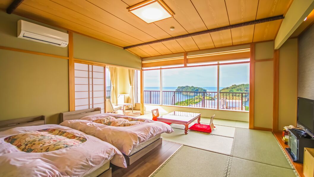 Een kamer met twee bedden, een televisie en uitzicht op zee.