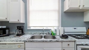 Une cuisine avec des armoires blanches, un évier à deux bacs, une cuisinière et un four à micro-ondes.