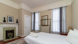 Une chambre à coucher avec un lit, une cheminée, un miroir et des rideaux.