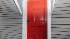 Une porte rouge dotée d’un clavier de code, intégrée dans une maison aux murs recouverts de bardage gris.