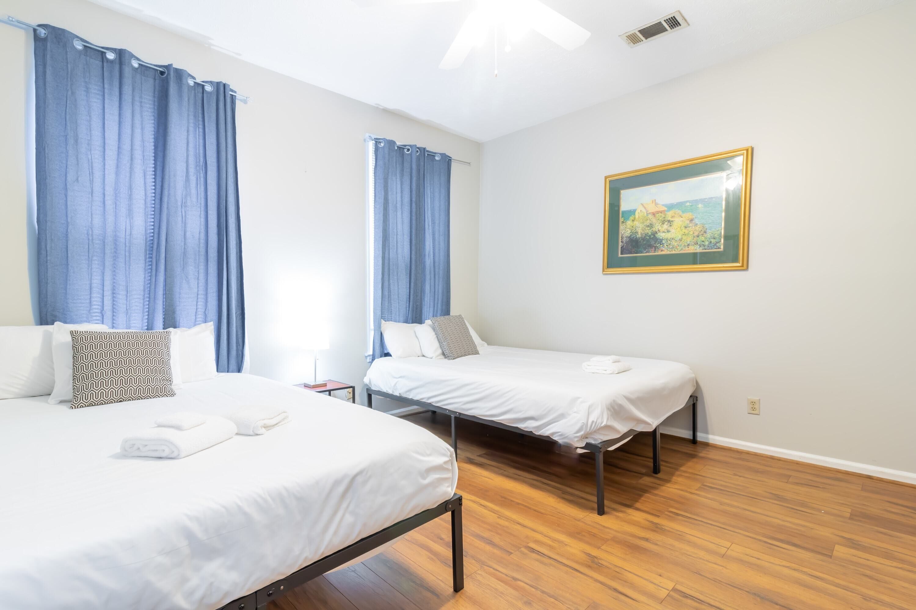 Une chambre d’hôtel avec deux lits simples, un tableau au mur et un plancher en bois.