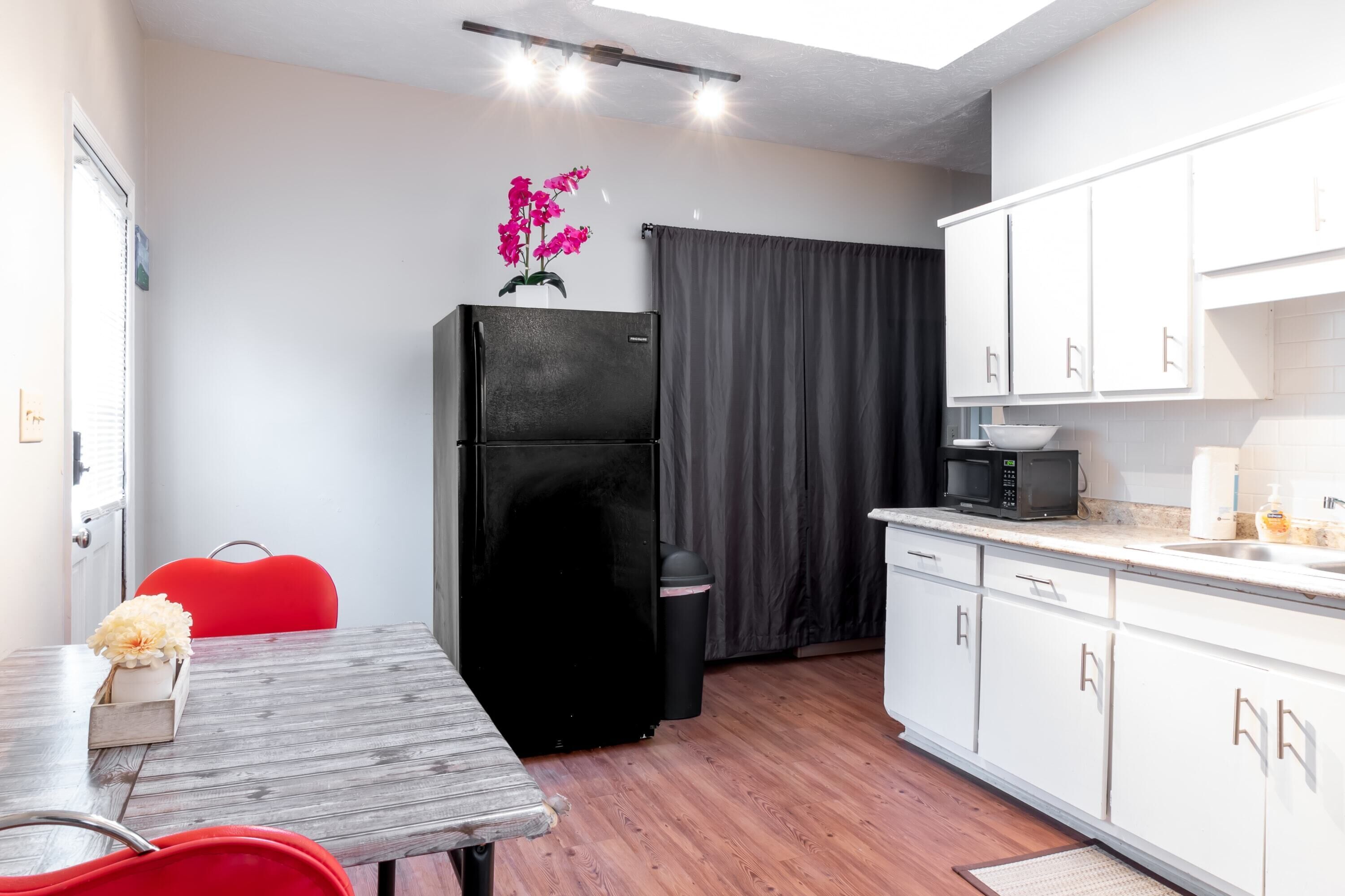 Cocina compacta con refrigerador, microondas y armarios blancos.