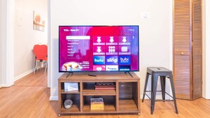 A flat-screen TV on a wooden stand with a shelf below, displaying a streaming service interface. - Pet-Friendly Duplex Near Riverwalk w/ Free Parking (Columbus)