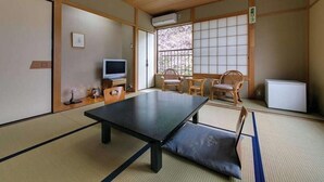 A tatami mat room with a low table, chairs, a television, and a refrigerator.
