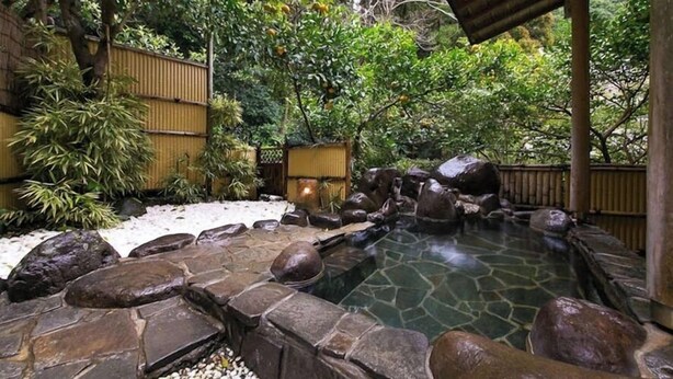 A stone-lined pool with rocks and a bamboo fence in a garden setting.