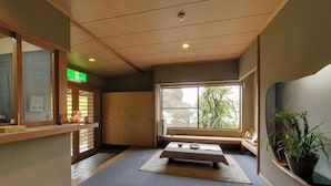 A room with a tatami mat, a low wooden table, a window with a view of trees, and a green exit sign.