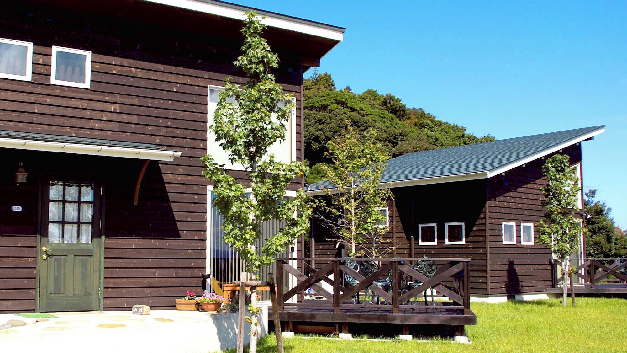 A wooden house with a green door, a small porch, and a grassy yard.