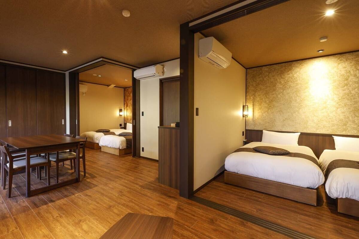 Habitación de hotel con piso de madera, un escritorio, dos camas y aire acondicionado instalado en la pared.