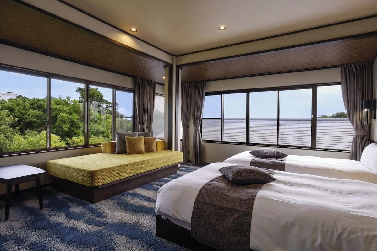 Habitación de hotel con una cama grande, un sofá cama más pequeño, un escritorio y vistas al mar.