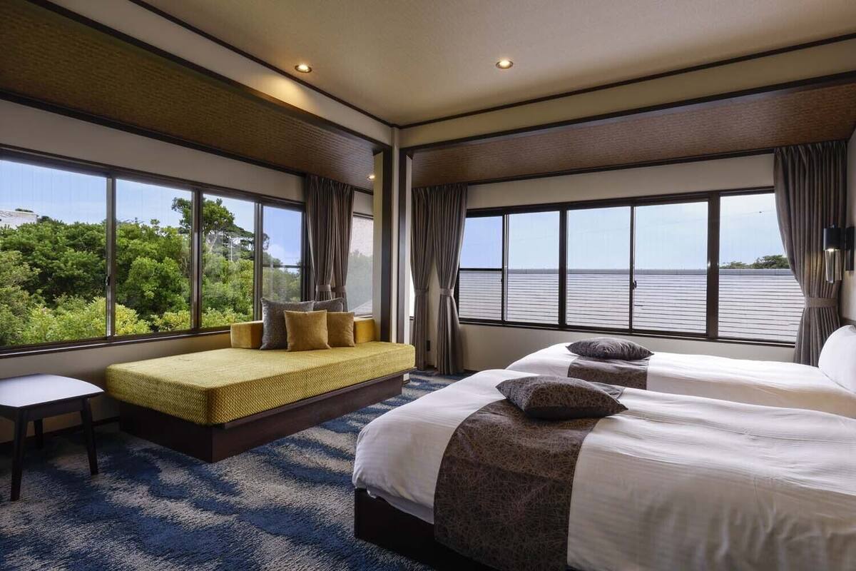 Una habitación de hotel con un ventanal grande, una cama, un sofá y una mesita.