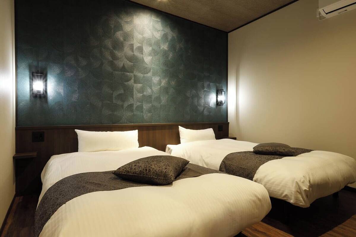 Habitación de hotel con dos camas, una pared oscura con textura y cabecero de madera.