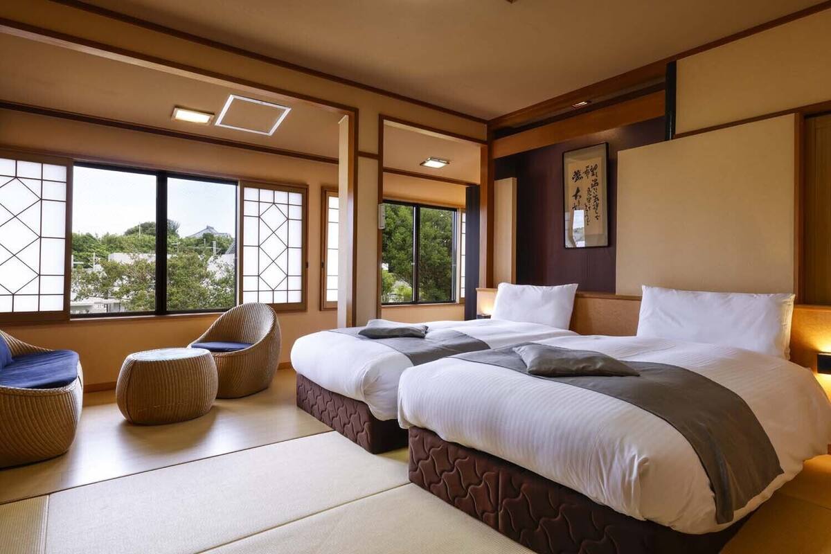 Habitación de hotel con dos camas, esteras de tatami, vistas a zonas verdes y decoración japonesa tradicional.