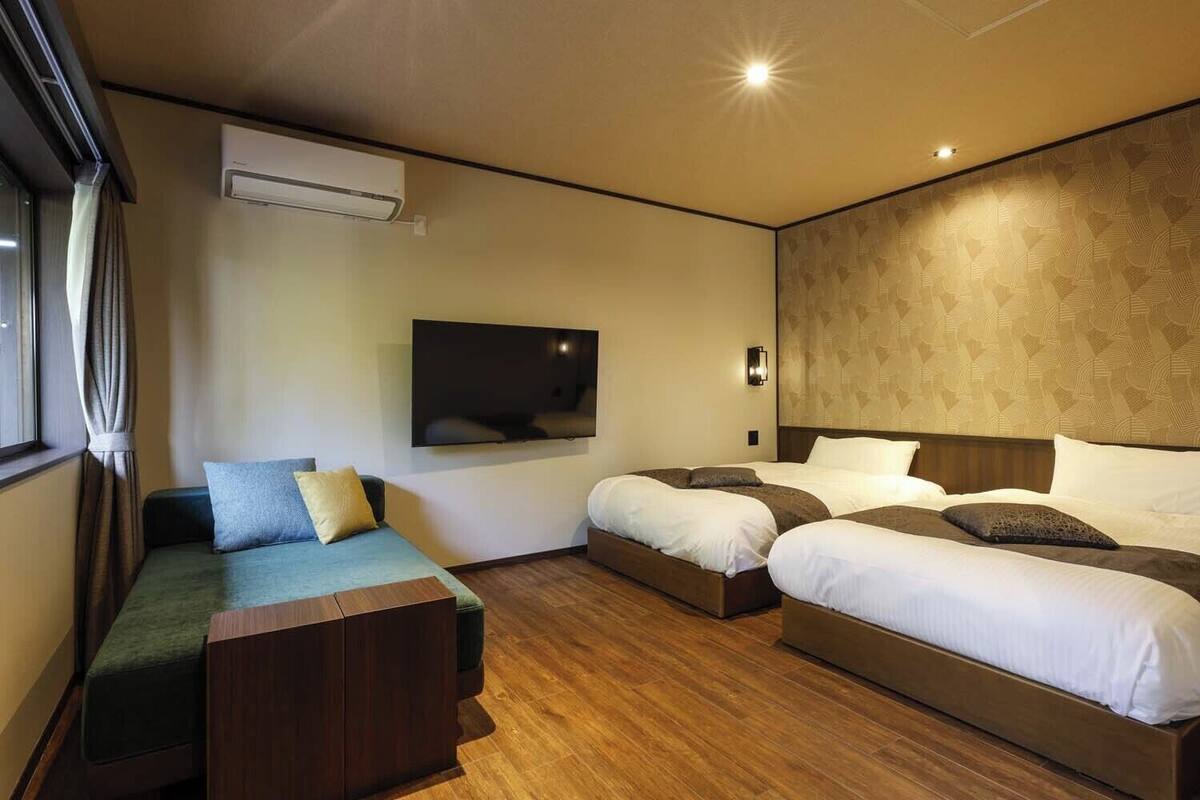 Una habitación de hotel con sofá, dos camas, televisión de pantalla plana y aire acondicionado.