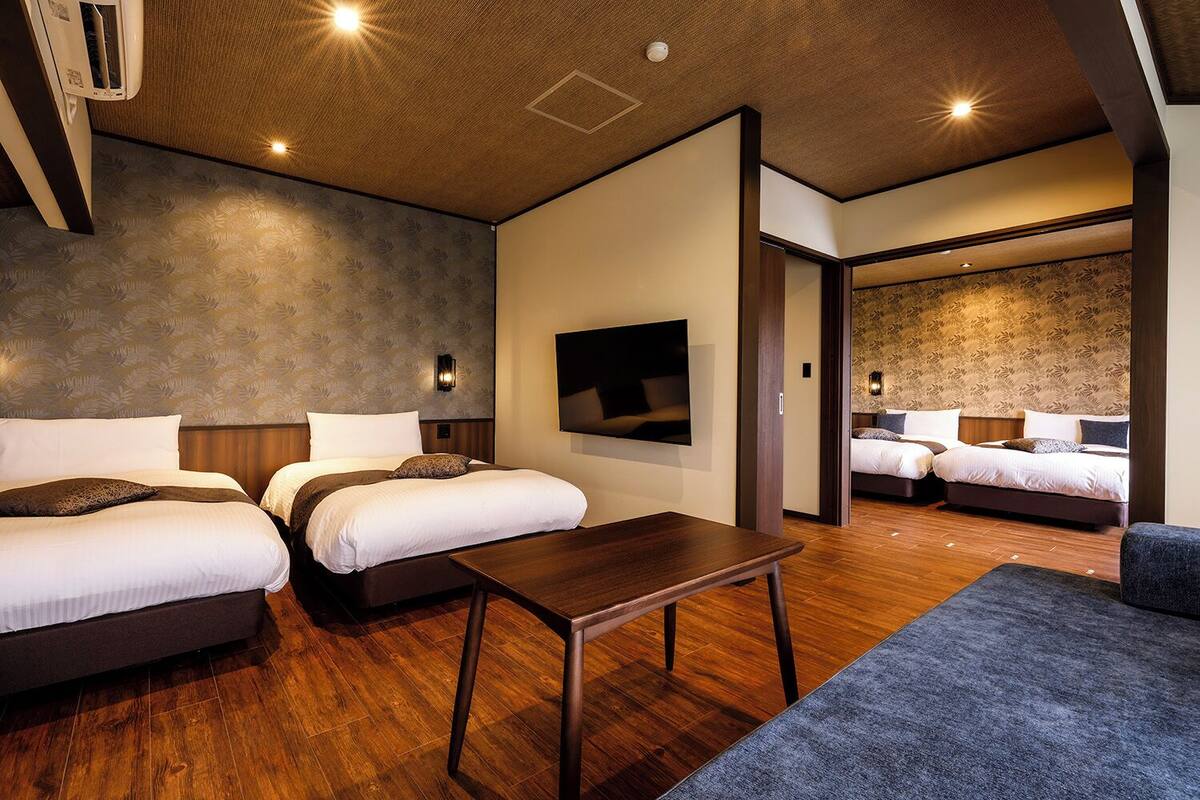Habitación de hotel con dos camas, televisión, mesa de madera y sofá.