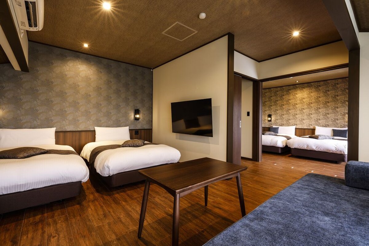 A hotel room with two beds, a flat-screen TV, a wooden table, and a sofa.