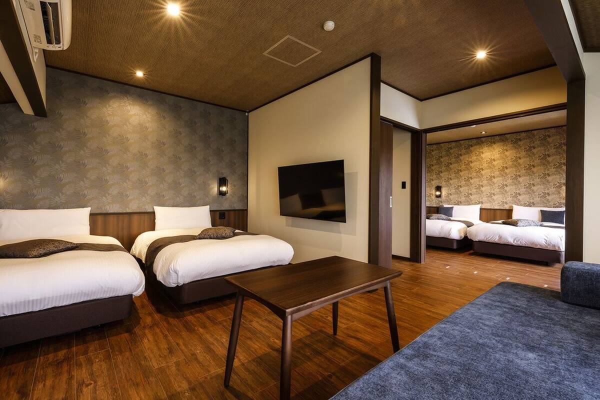 Una habitación de hotel con dos camas, un televisor de pantalla plana, una mesa de madera y un sofá.