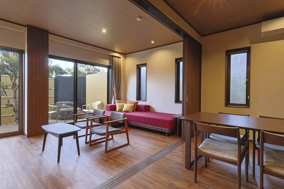 Un interior moderno con suelo de madera, un sofá rojo, una mesa de comedor y un amplio ventanal.