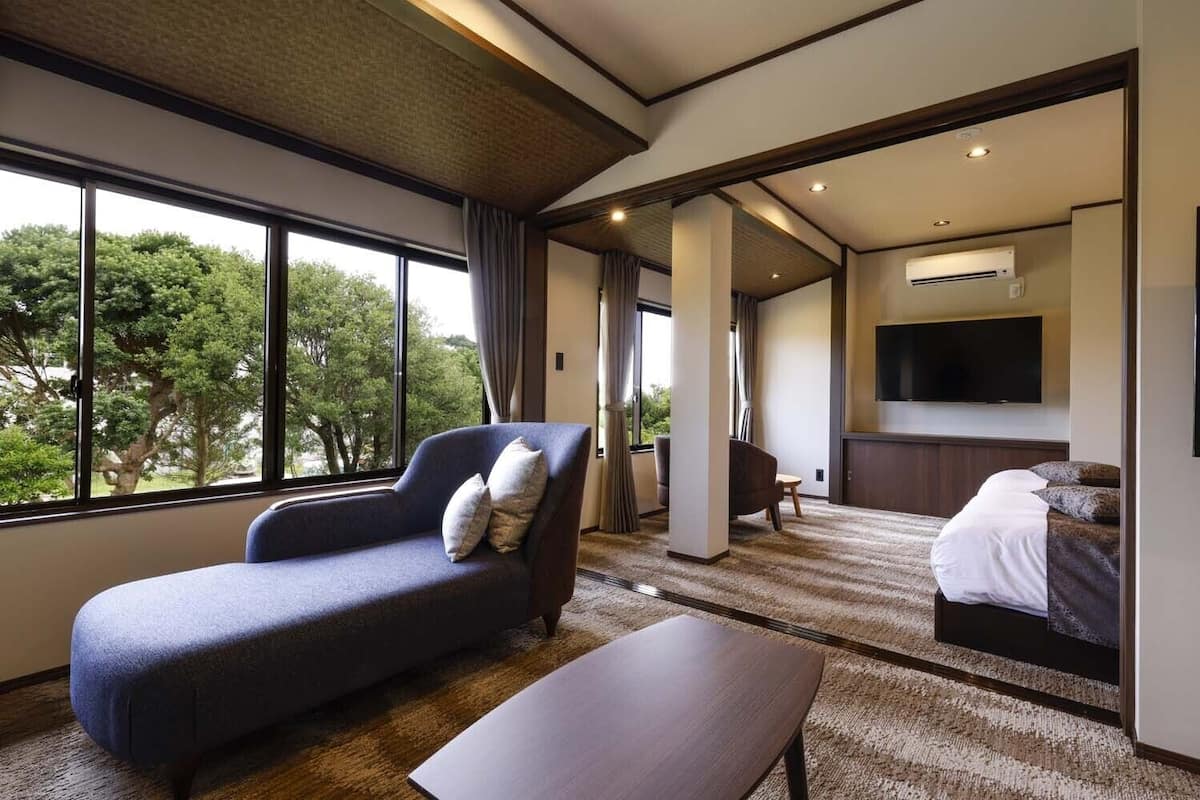 Habitación de hotel con sofá, cama, televisión y vistas a árboles.