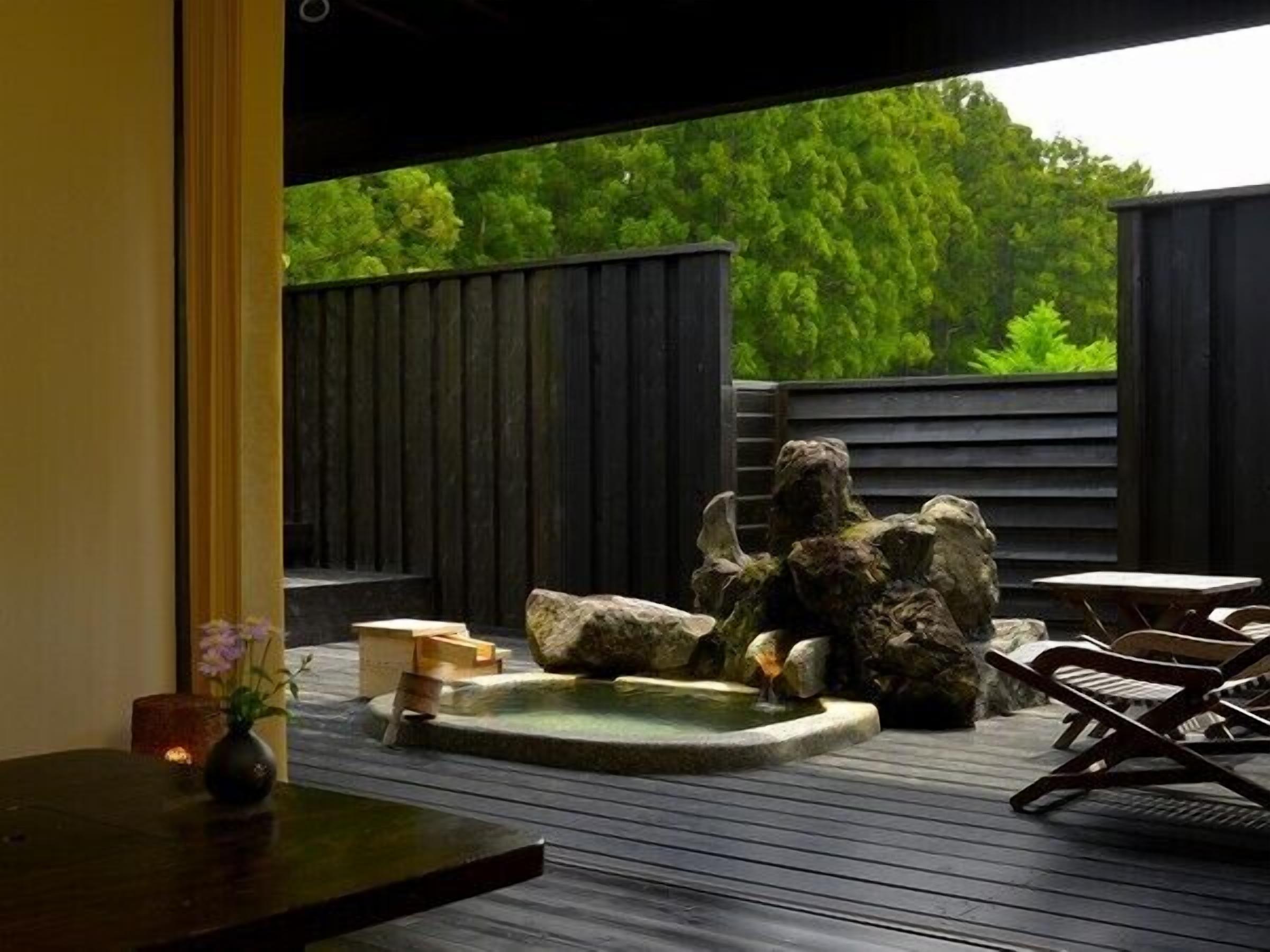 A wooden deck with a hot spring, rocks, and a table with chairs.