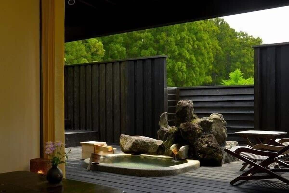 A wooden deck with a hot spring, rocks, and a table with chairs.