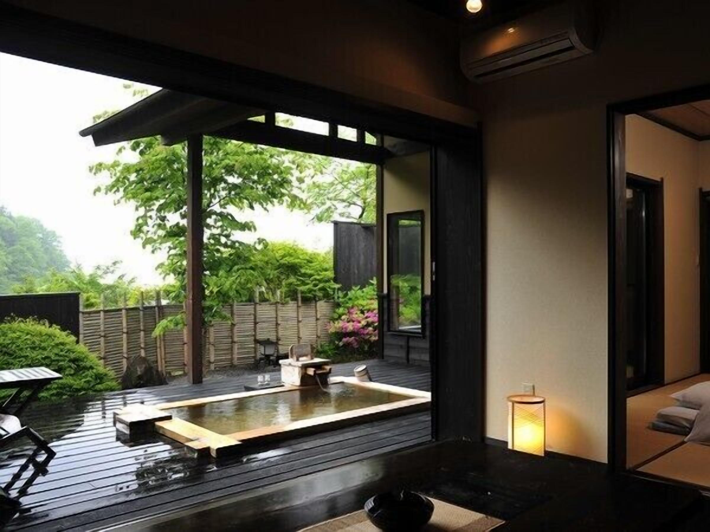 A modern Japanese-style room with tatami flooring, a traditional tea ceremony area, and a view of a lush garden.