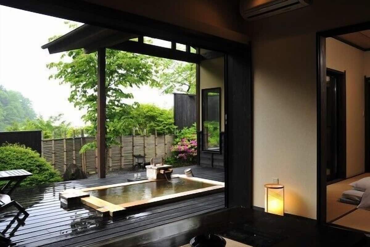 A modern Japanese-style room with tatami flooring, a traditional tea ceremony area, and a view of a lush garden.