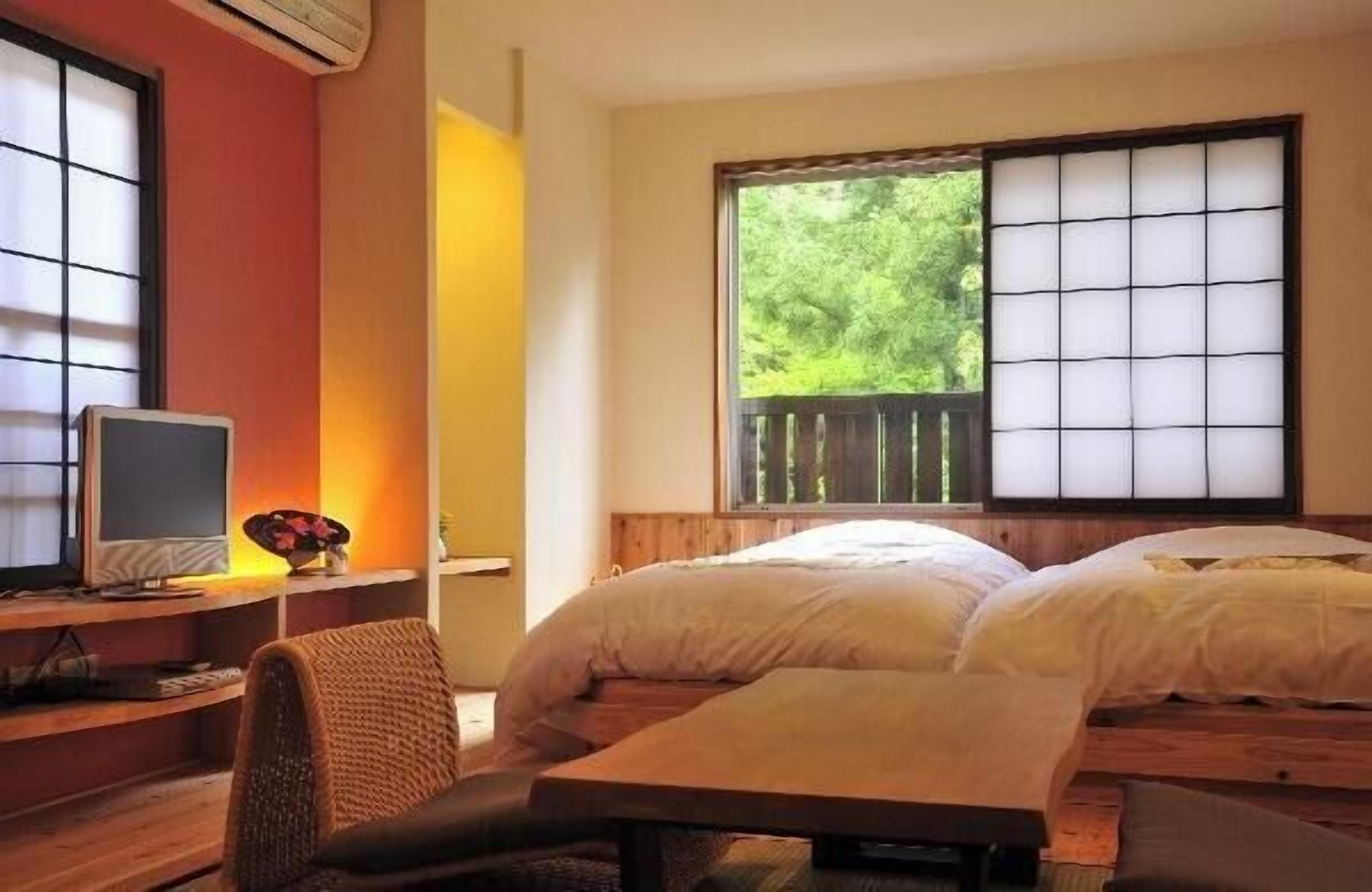 A room with a bed, a desk with a computer, and a window with a view of trees.