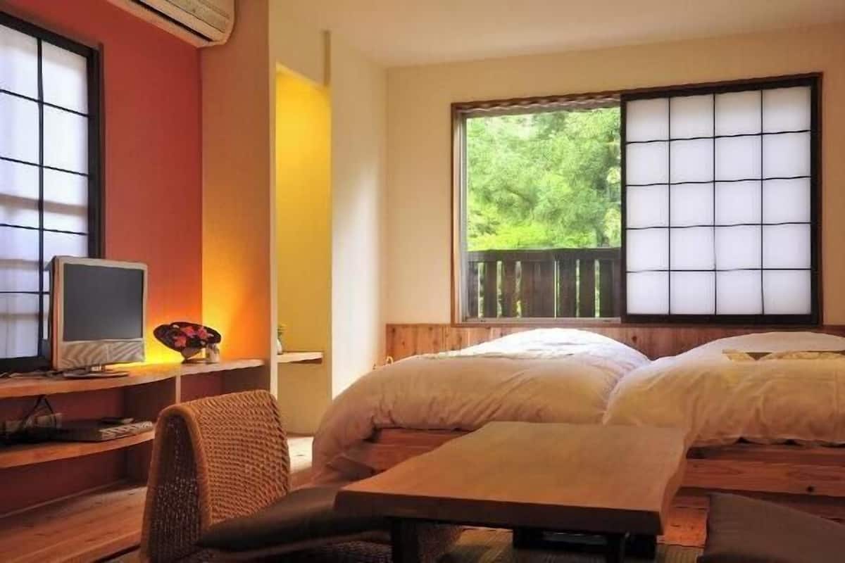 A room with a bed, a desk with a computer, and a window with a view of trees.