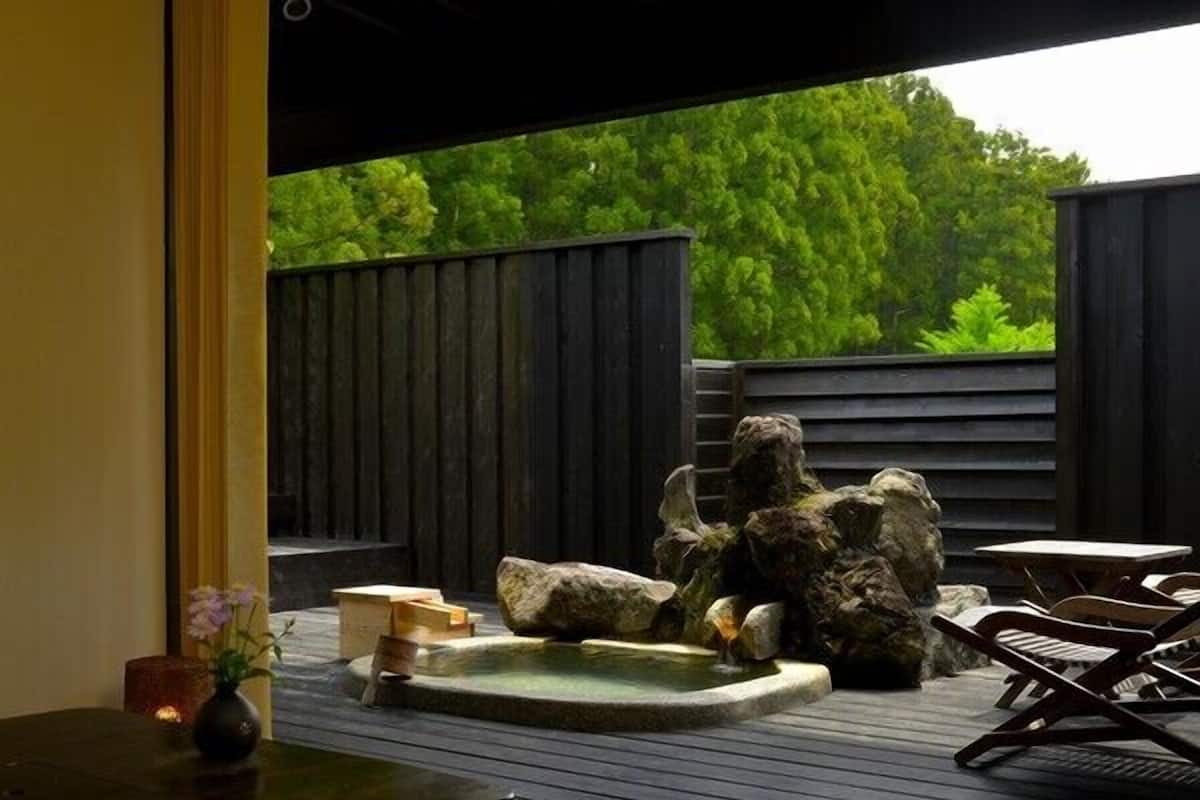 A wooden deck with a hot tub, rocks, and lounge chairs.