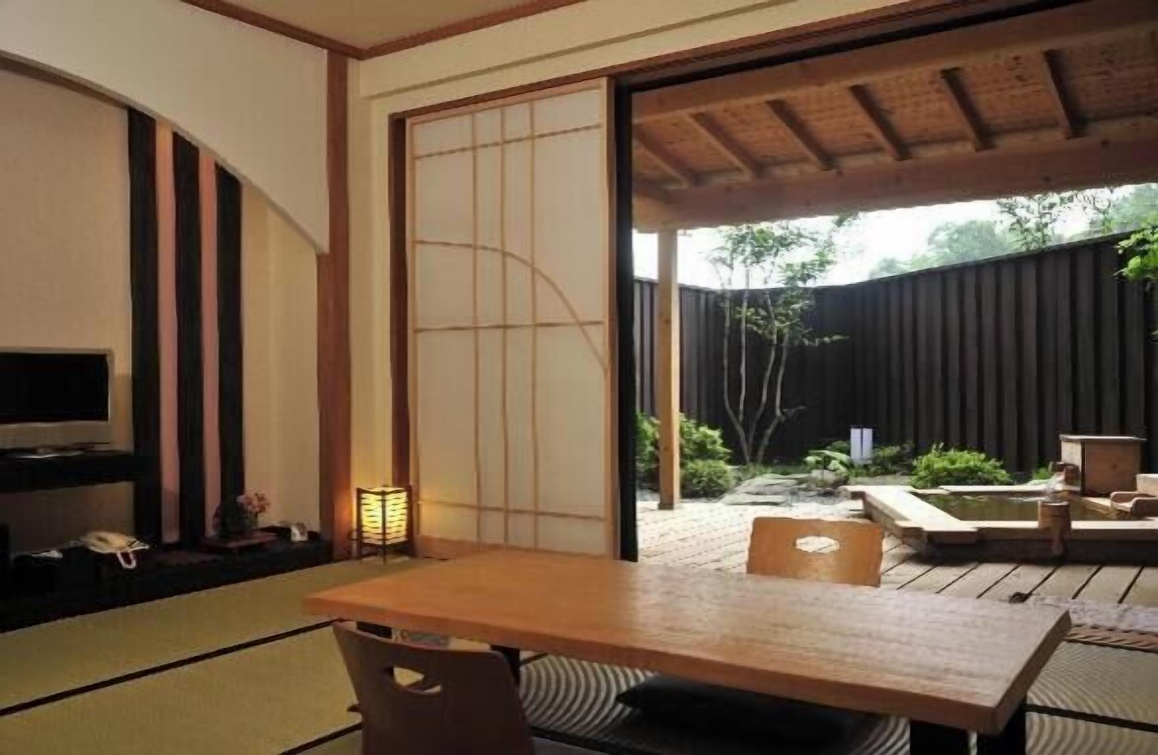 A traditional Japanese room with tatami flooring, a low table, a television, and a sliding door leading to an outdoor garden.