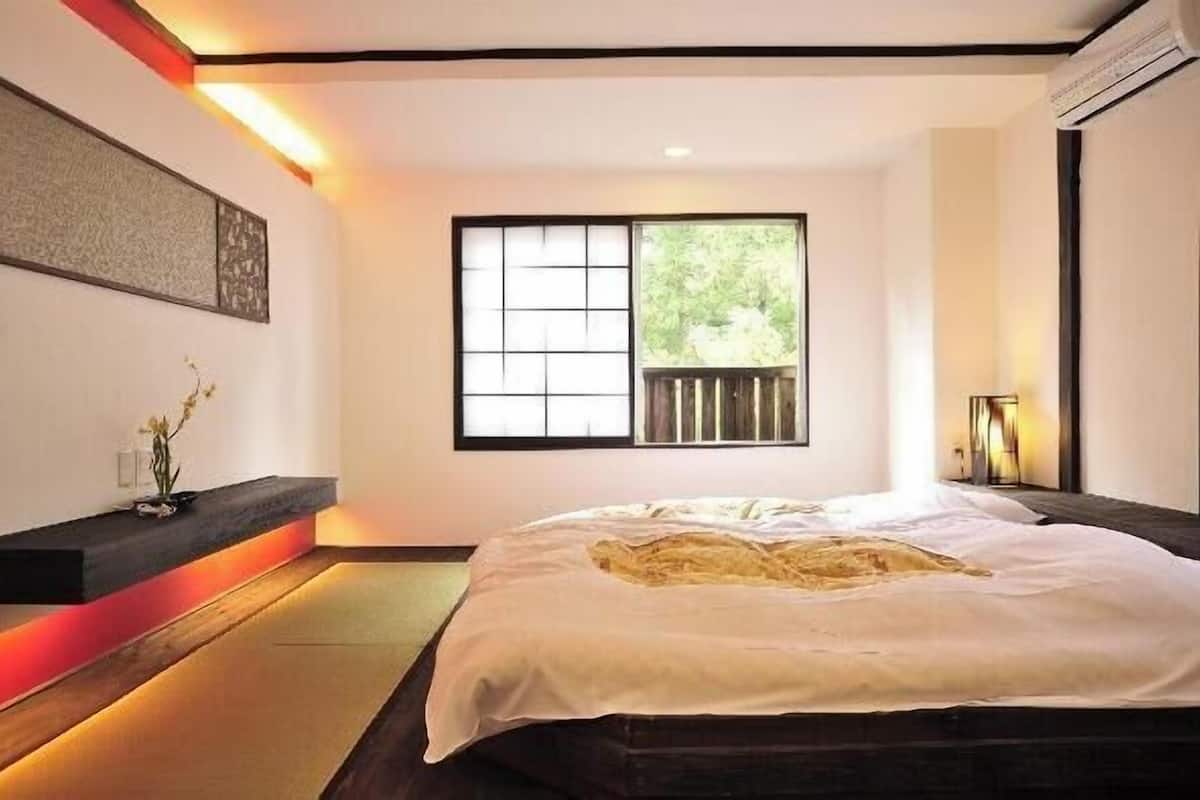 A bedroom with a bed, a window, a wall-mounted shelf with a vase, and a bedside table.