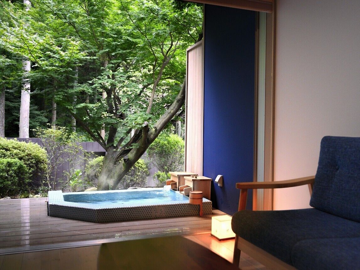 A hot tub on a wooden deck with a view of trees and a blue wall.