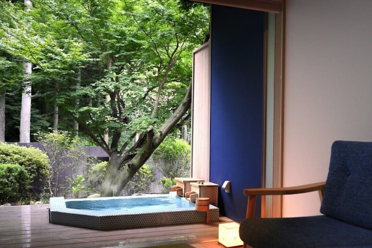 A hot tub on a wooden deck with a view of trees and a blue wall.