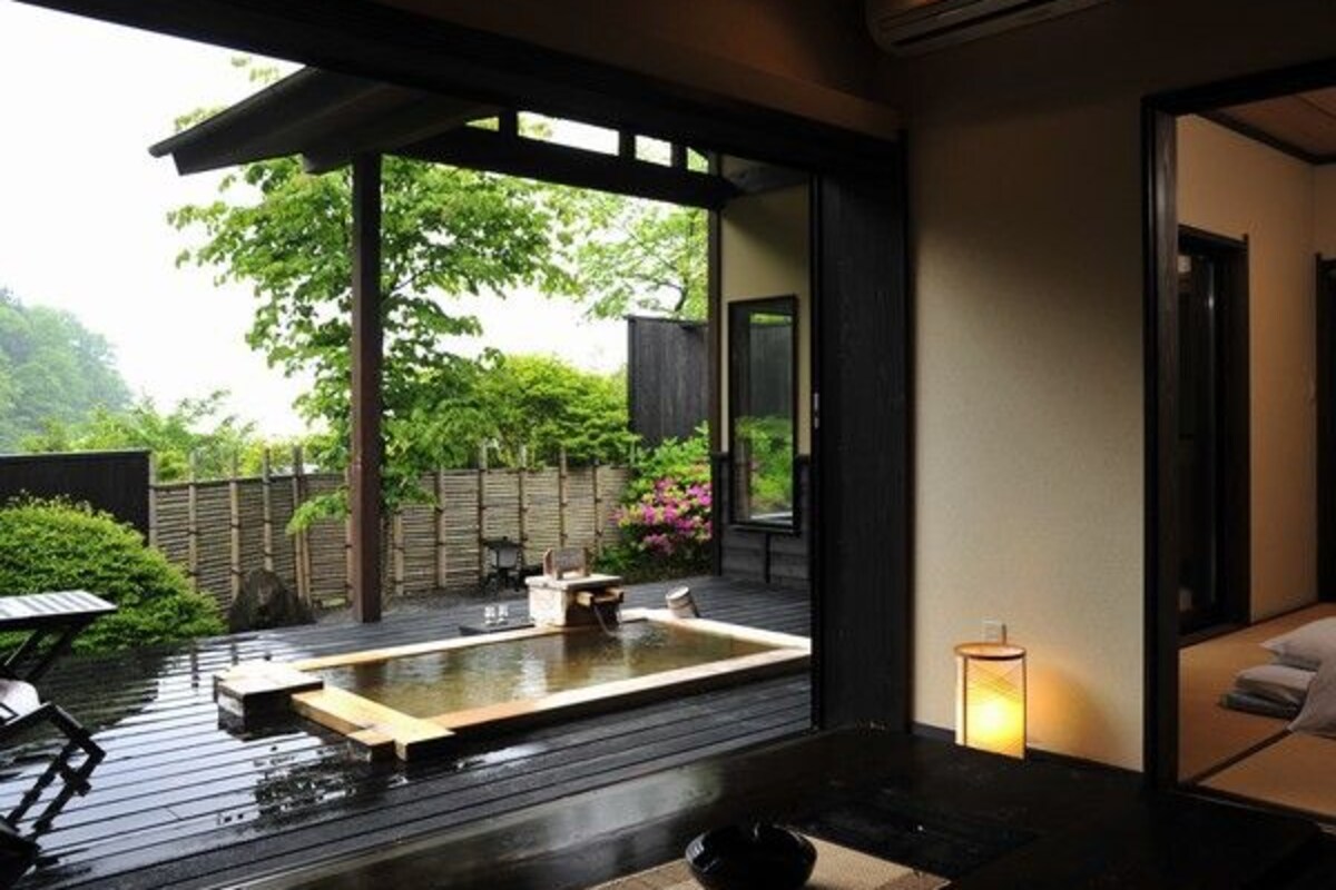 A modern Japanese-style room with tatami flooring, a traditional tea ceremony area, and a view of a lush garden.