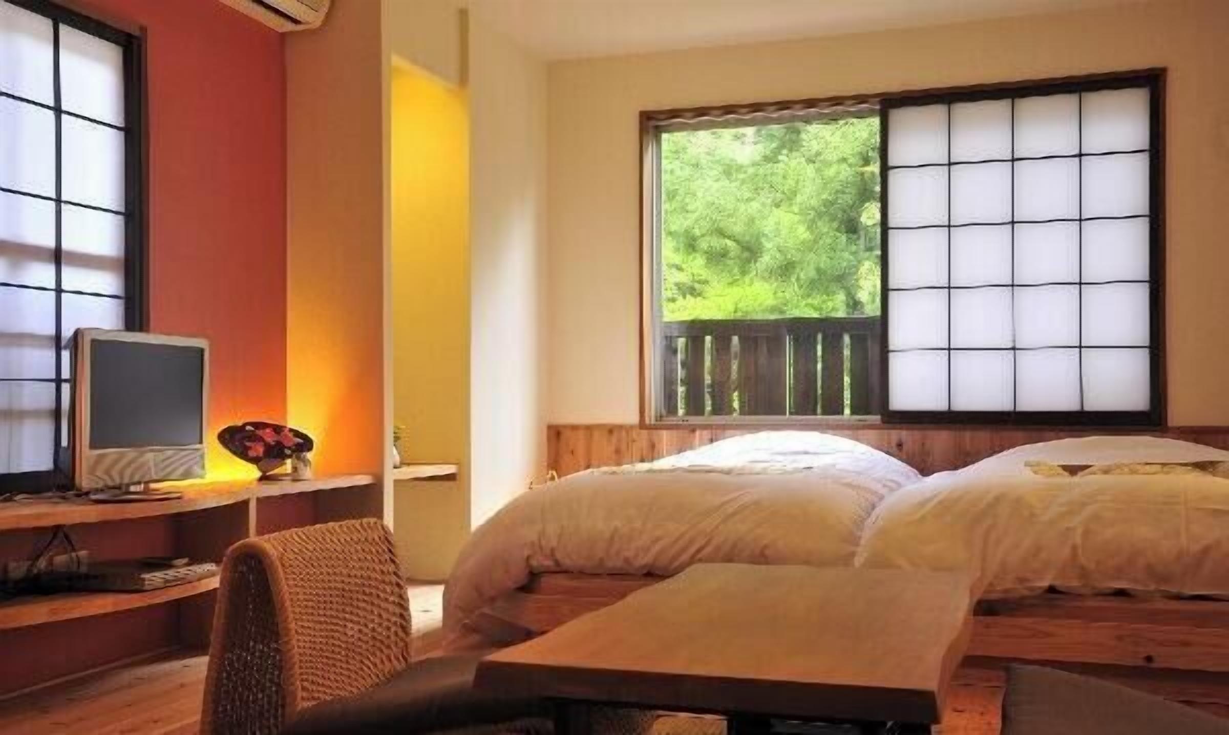 A room with two beds, a desk with a computer, and a window with a view of greenery.