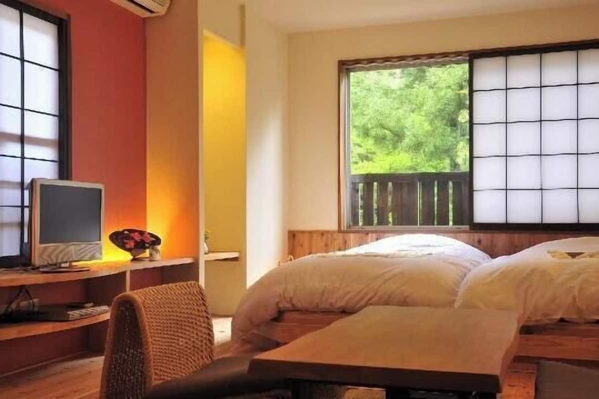 A room with two beds, a desk with a computer, and a window with a view of greenery.