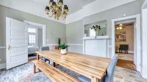 Een eetgedeelte met een houten tafel en banken, een kroonluchter en een spiegel boven de tafel.
