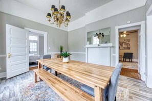 A dining area with a wooden table and benches, a chandelier, and a mirror above the table. - Near Parks Downtown & Riverwalk: Midtown Muse Sleeps 14 (Columbus)