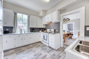 A modern kitchen with white cabinets, a built-in oven, and a large window. - Near Parks Downtown & Riverwalk: Midtown Muse Sleeps 14 (Columbus)