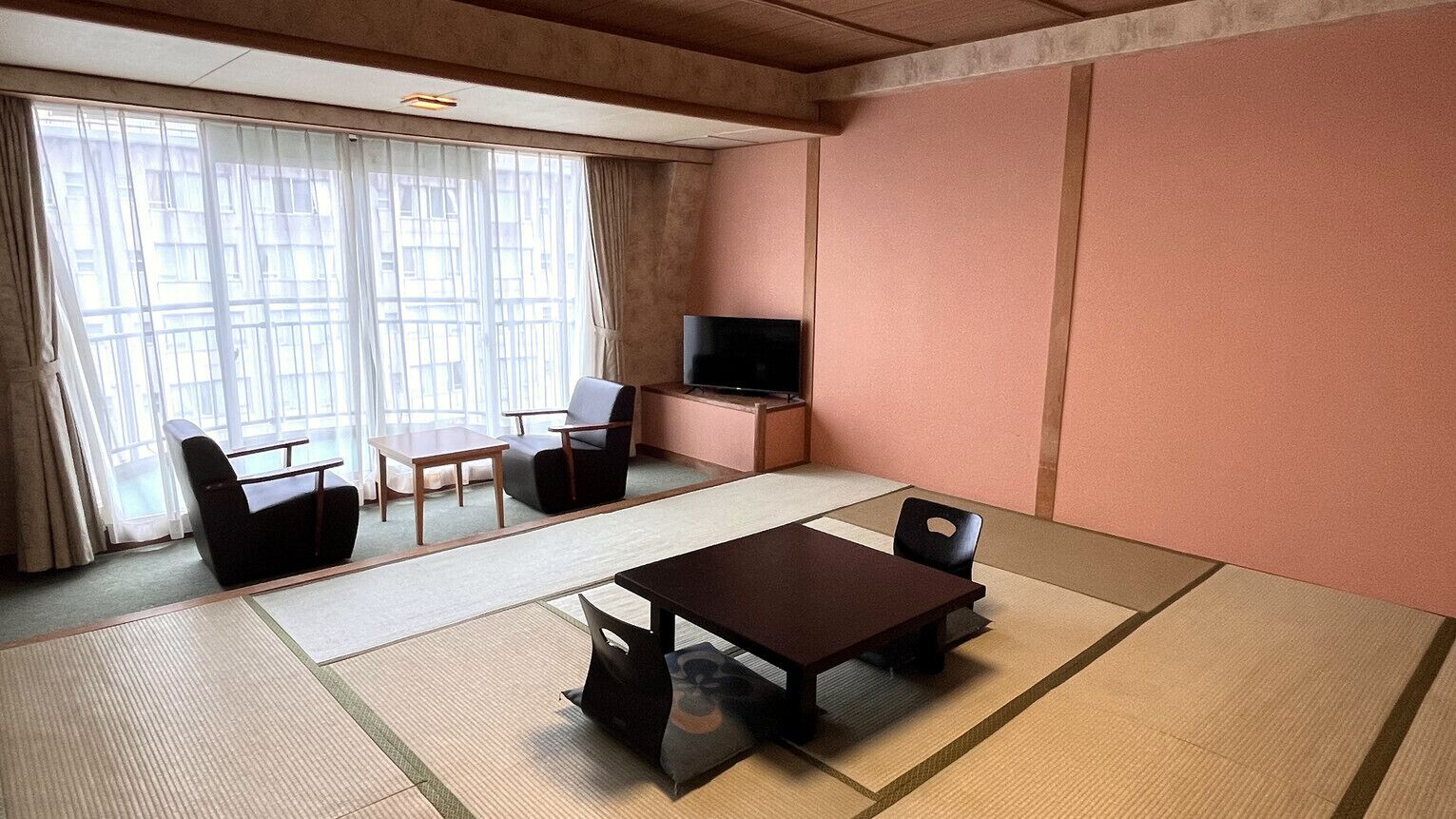 A room with tatami flooring, a television, a sofa, and a table.