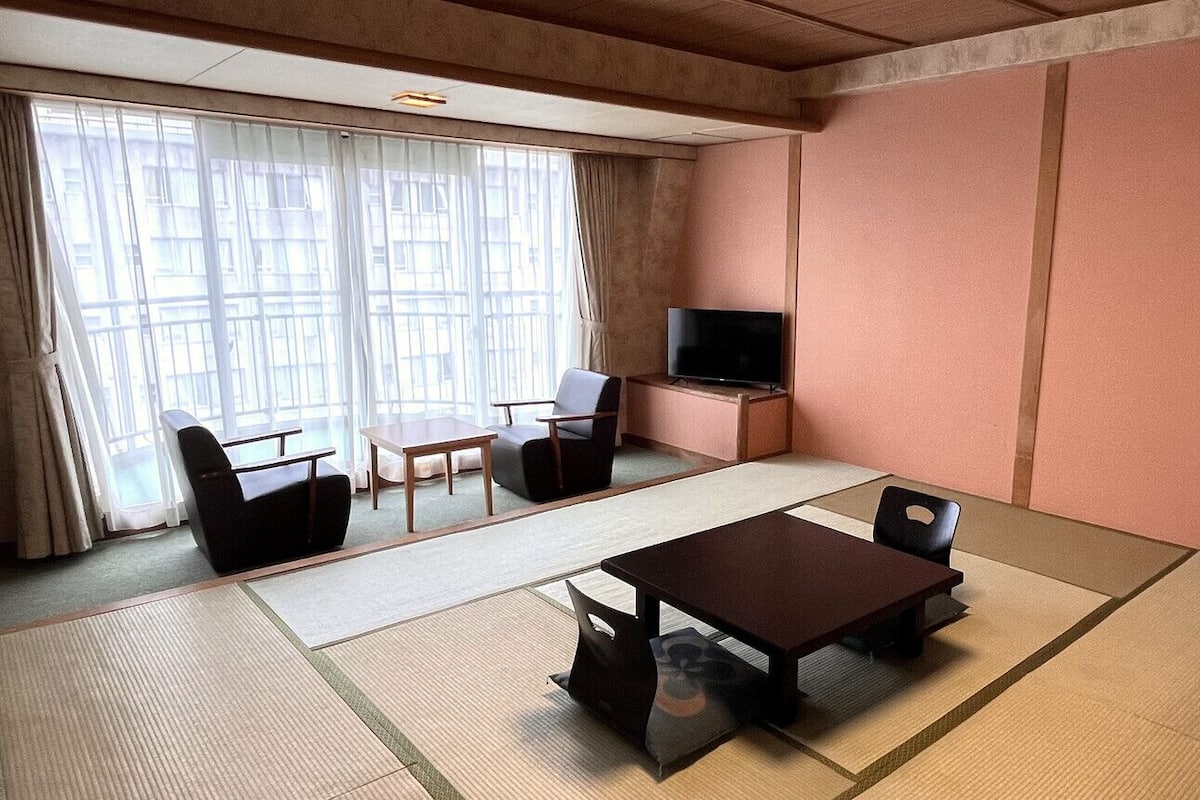 A room with tatami flooring, a television, a sofa, and a table.