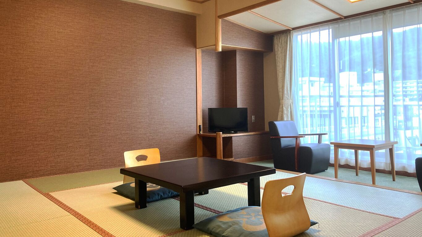 A room with tatami flooring, a television, a table, and chairs.