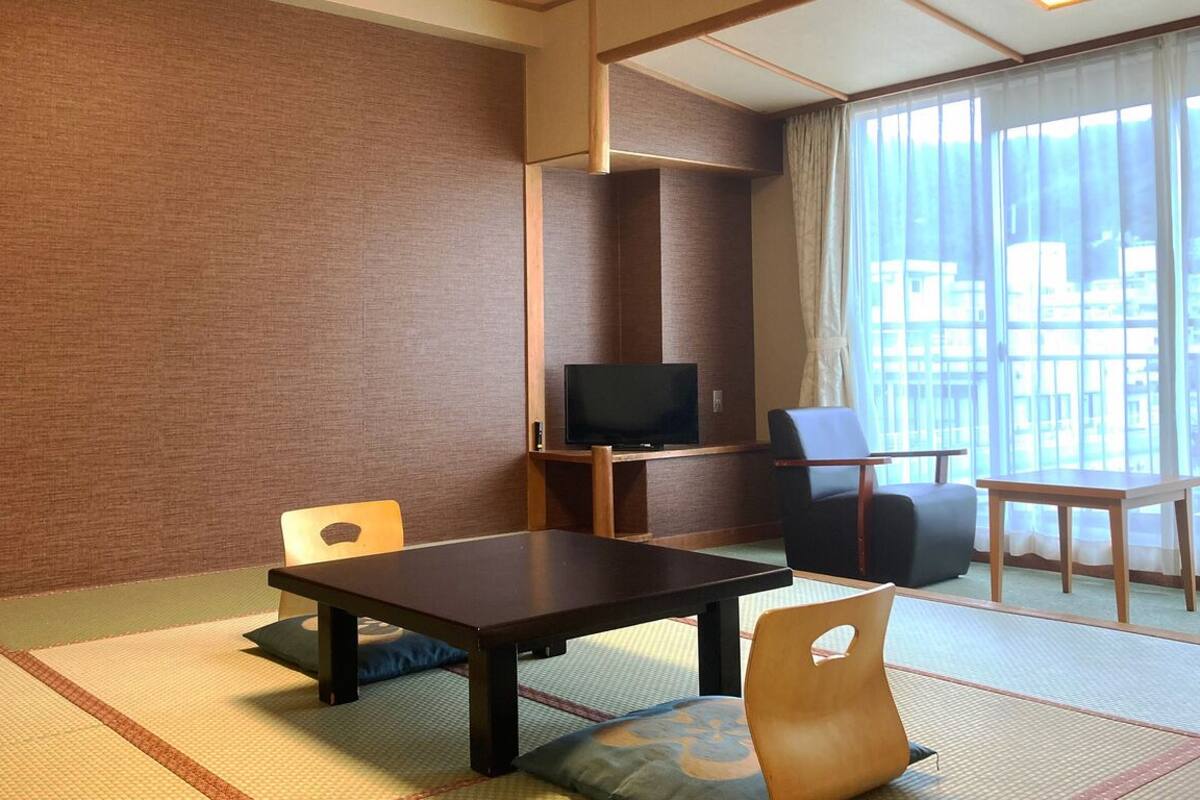 A room with tatami flooring, a television, a table, and chairs.