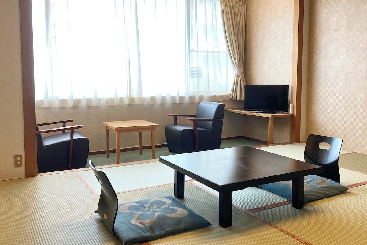 A traditional Japanese room with tatami flooring, a low table, a sofa, a chair, and a television.